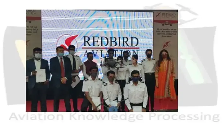 Group photo of masked trainees and staff at a RedBird Aviation certification ceremony, holding certificates and a drone on stage