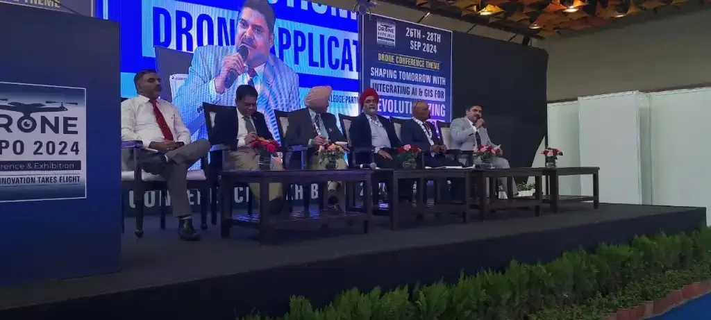 Panel of speakers seated on stage discussing drone applications at Drone Expo 2024, one speaker at the microphone