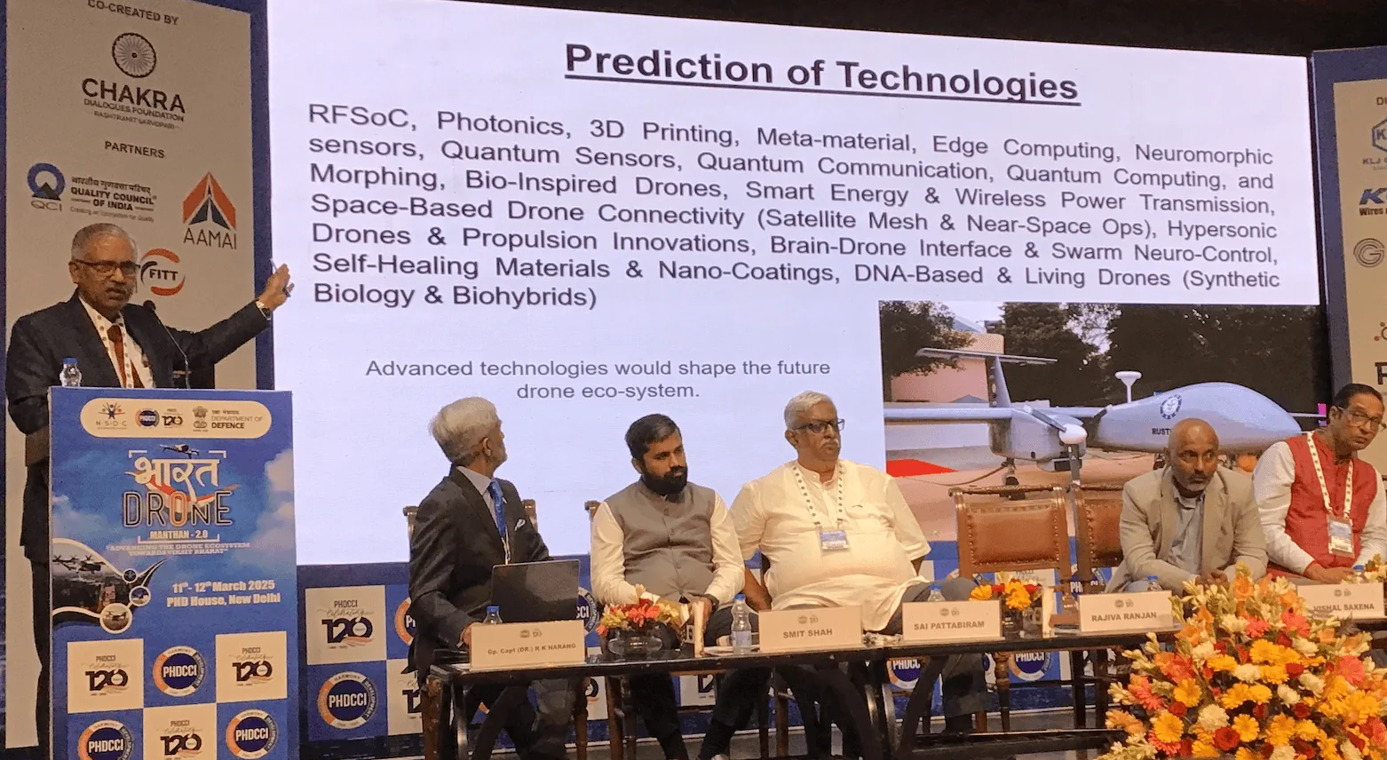 Conference panel discussing prediction of future drone technologies such as RFSoC, photonics, quantum sensors and bio-inspired drones, with a Rustom UAV shown on screen