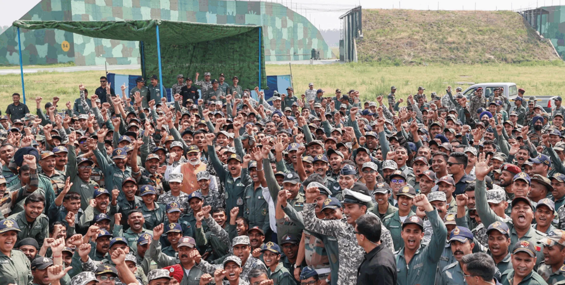 Prime Minister Narendra Modi standing among a large group of cheering armed forces personnel with fists raised at a military base